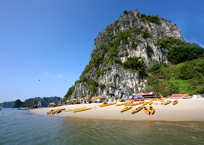 Bãi biển cát trắng với hàng cây kayak màu vàng và nền là một vách đá lớn.